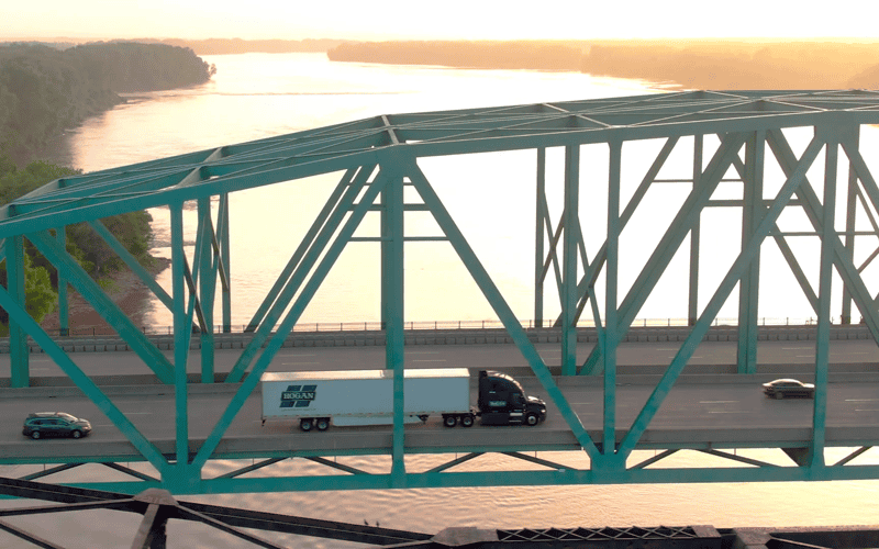 A Hogan truck traveling over a bridge at sunset.