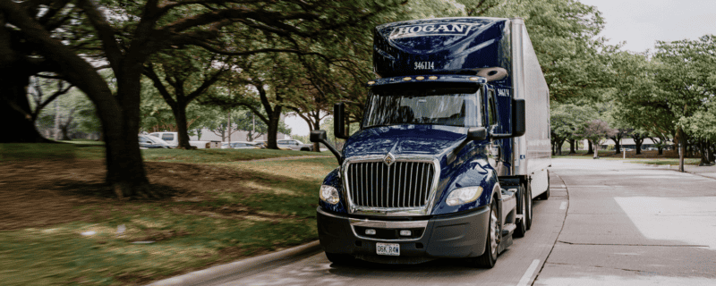 A blue Hogan truck driving down a tree-lined street.