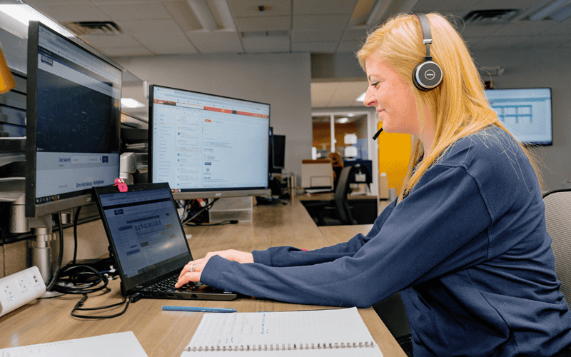 A woman at Hogan corporate wearing a headset and talking on the phone with a customer.