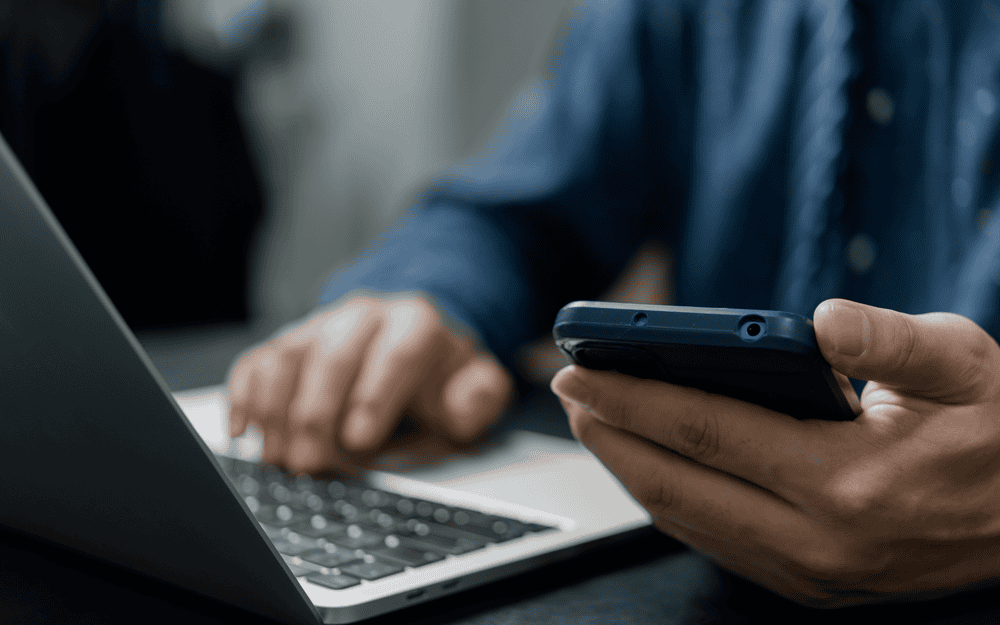 A close up of a man on his phone and laptop.